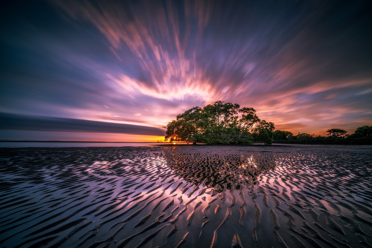 En Sie ein Bild, das einen lebendigen Sonnenuntergang über einem ruhigen Strand zeigt, wobei warme Farbtöne den Himmel dominieren und allmählich von feurigem Rot zu beruhigendem Orange und sanftem Gelb übergehen, um das Konzept der Farbtemperatur und ihre Bedeutung zu veranschaulichen in der visuellen Wahrnehmung